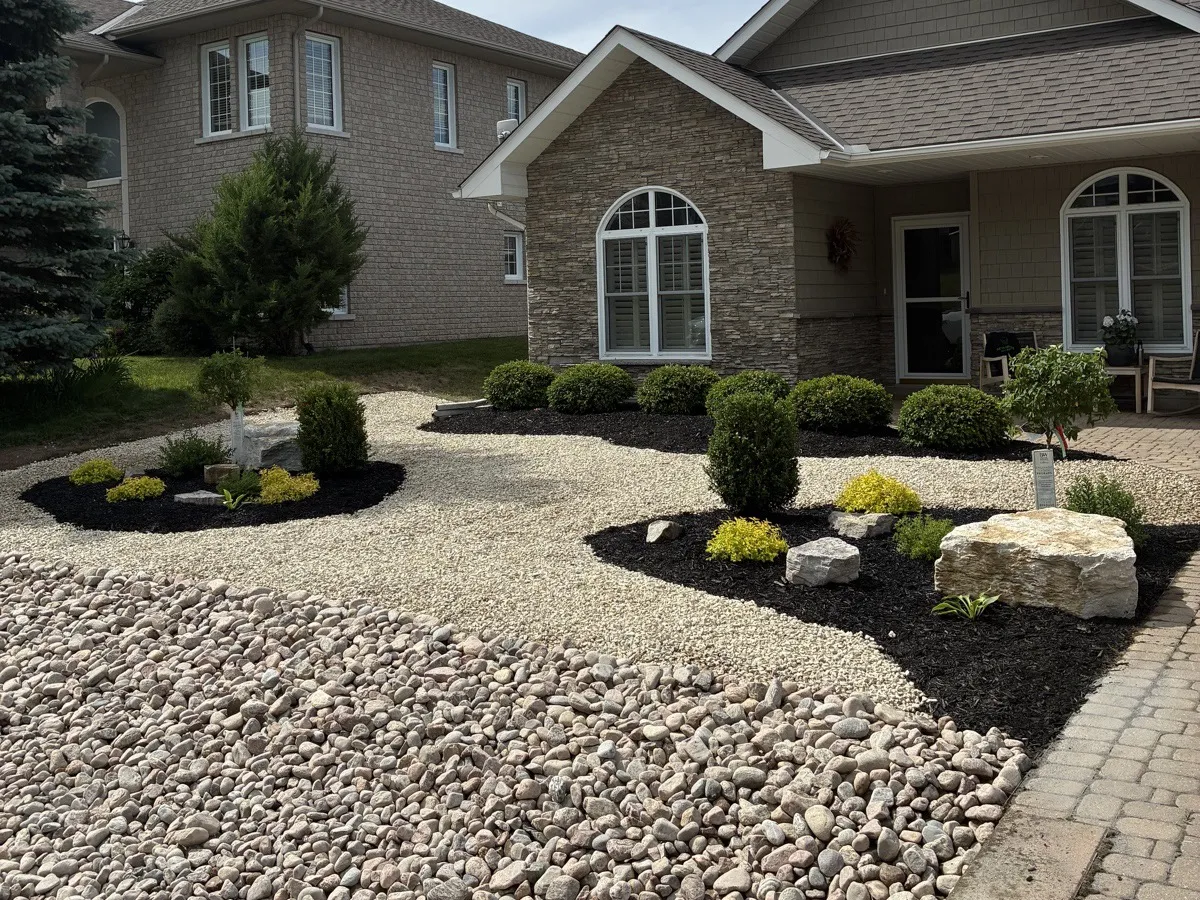 Front yard with river rock, mulched garden beds, shrubs, and armour stone accents, landscaped by Martin Services